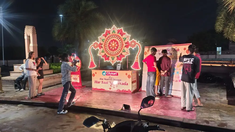 Visitors photographing and writing wishes at the lit Citykart Rakhi activation at night in Lucknow