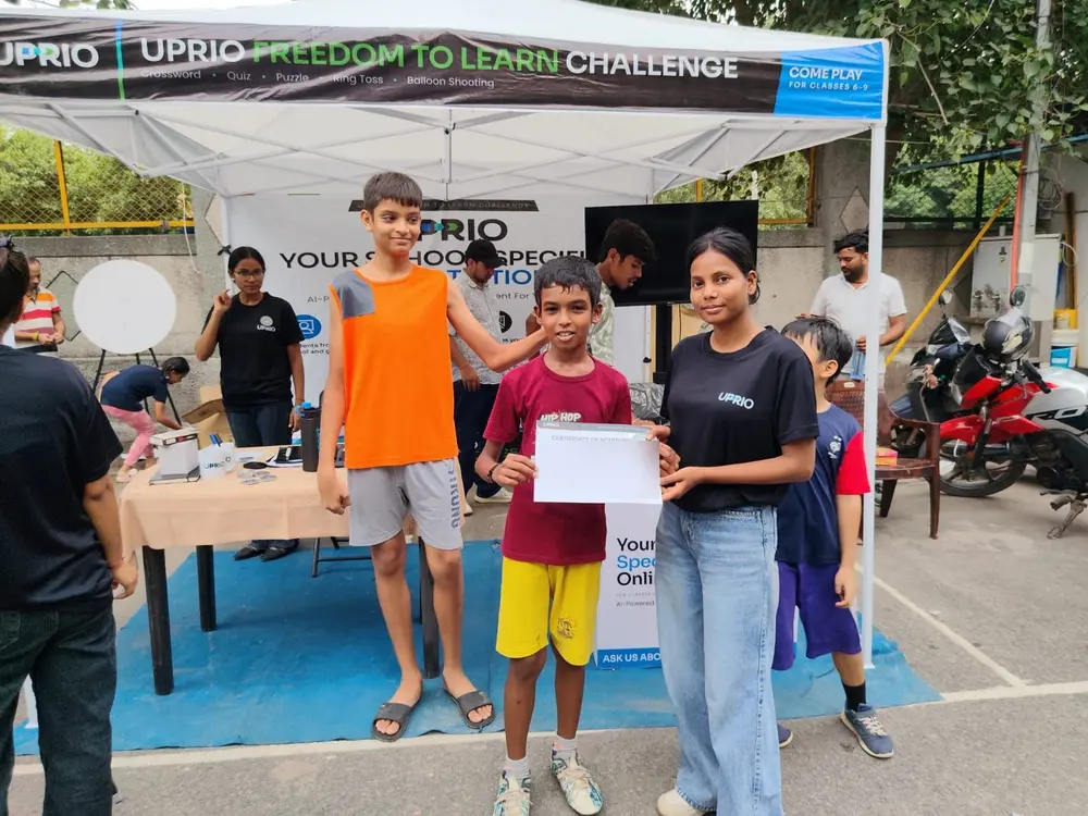 A child receiving a UPRIO-branded certificate from a promoter at the Freedom to Learn Challenge stall